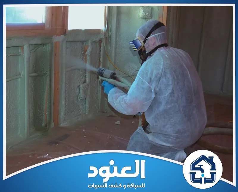 شركة عزل الحوائط بالفوم ببقعاء 0534999675 شركة العنود عامل يرتدي ملابس واقية ويستخدم جهاز رش لتطبيق العزل على جدران المبنى.